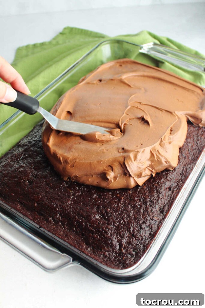 Spreading chocolate cream cheese frosting evenly over a freshly baked chocolate zucchini cake.