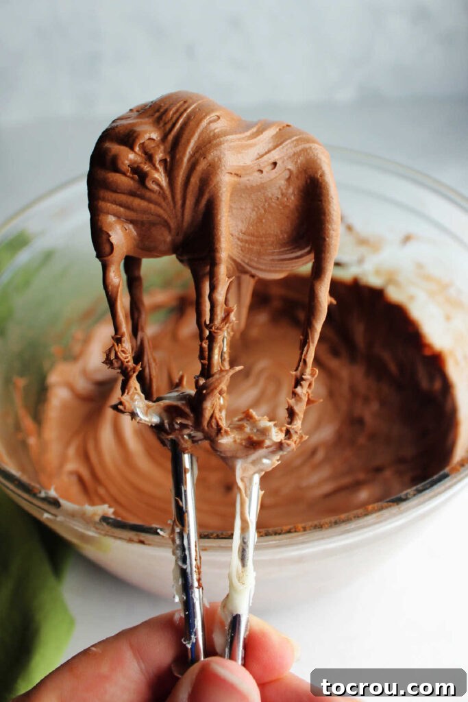 Decadent Chocolate Cream Cheese Frosting 5 Beaters from an electric mixer held up with creamy chocolate cream cheese frosting in them.