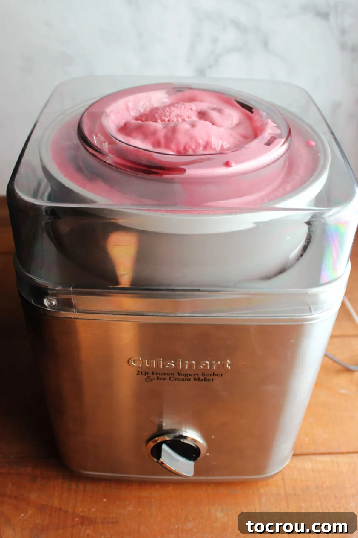 A vibrant pinkish-purple blackberry ice cream swirls within an ice cream maker, signifying it's freshly churned and almost ready to be transferred to storage containers for freezing.