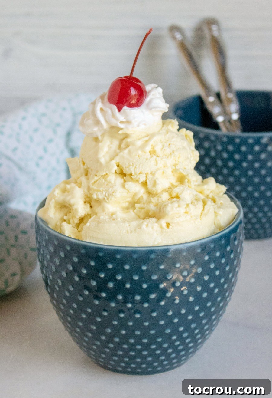 A vibrant bowl of lemonade ice cream, perfectly scooped and generously topped with a swirl of whipped cream and a bright red cherry, presented against a soft, blurred background.