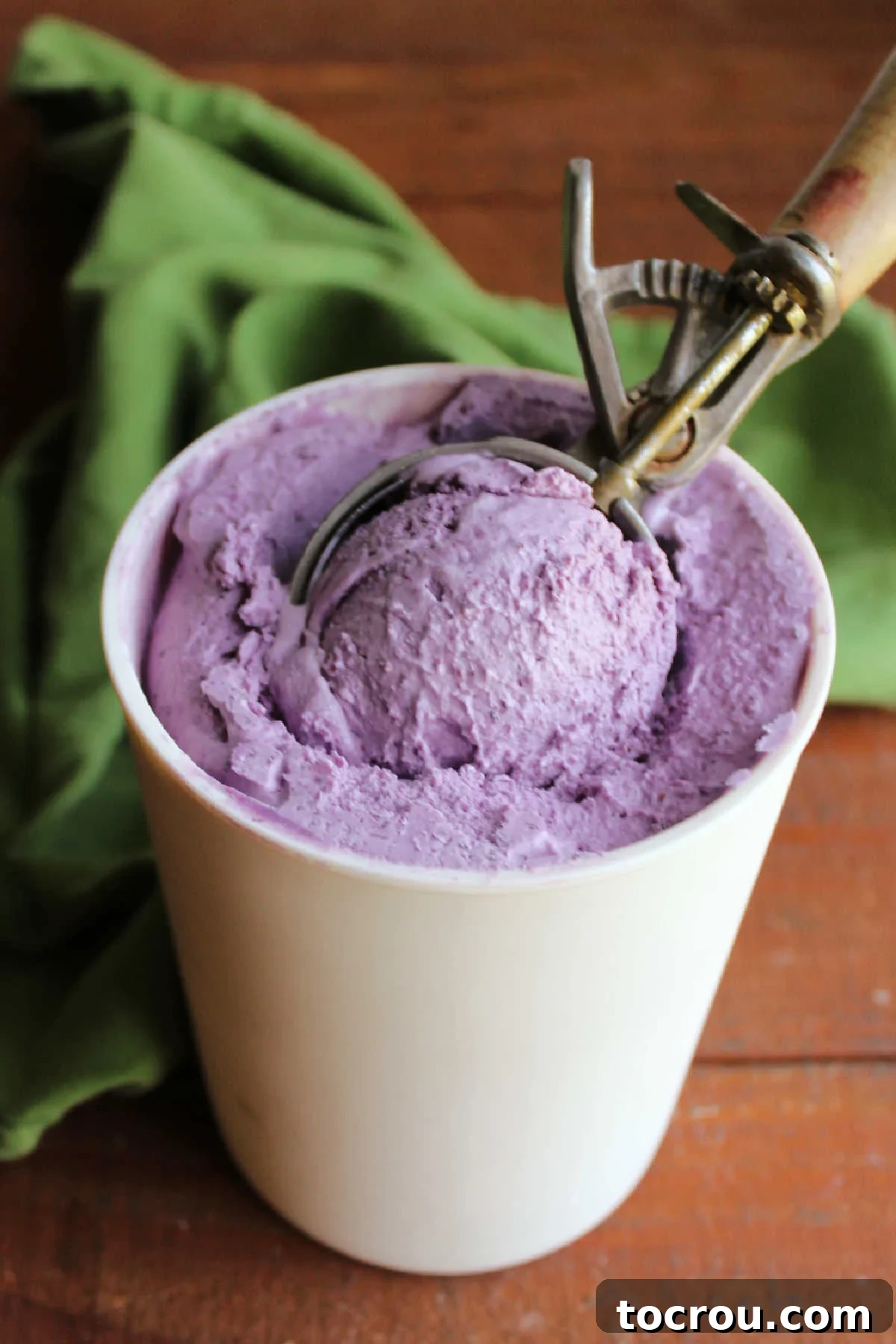 An antique ice cream scoop, possibly a family heirloom, gracefully retrieves a perfect ball of vibrant blueberry ice cream from a chilled freezer container, showcasing a rich, deep purple hue.