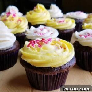 Rich chocolate cupcakes decorated with white and yellow condensed milk buttercream and pink and white sprinkles.