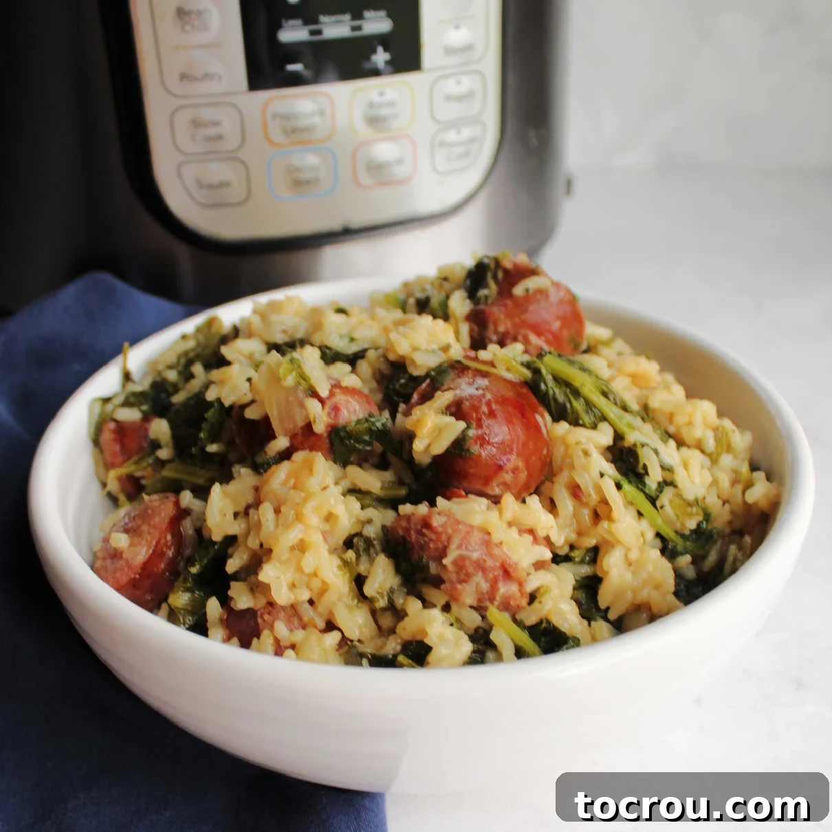 A steaming bowl of fluffy rice mixed with slices of savory kielbasa sausage and vibrant, wilted mustard greens, perfectly cooked and ready to eat. An Instant Pot is visible in the background, highlighting the ease of preparation.