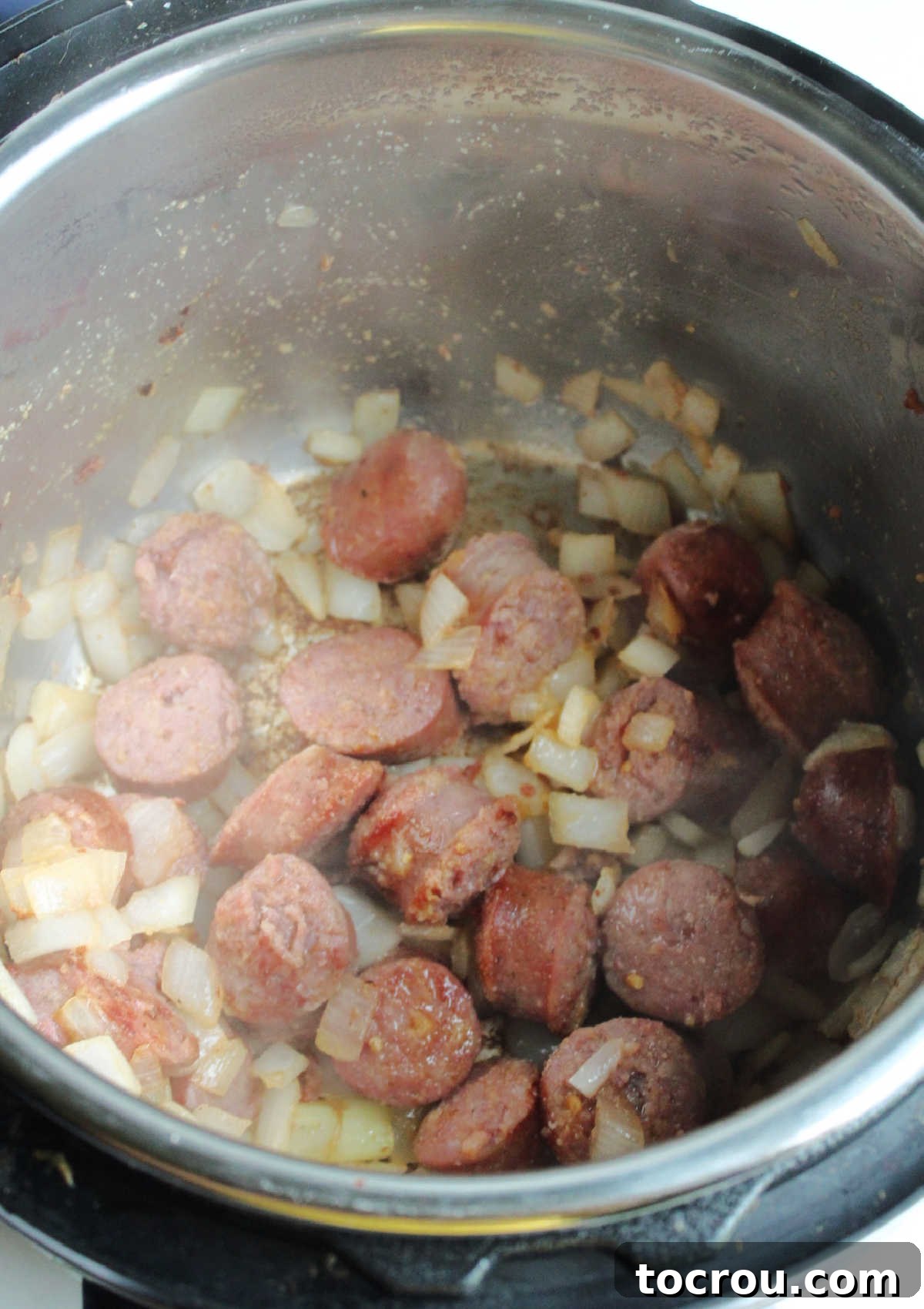 An overhead view inside an Instant Pot, showing perfectly browned pieces of kielbasa sausage mingled with softened, translucent diced onions, creating a fragrant base for the meal.
