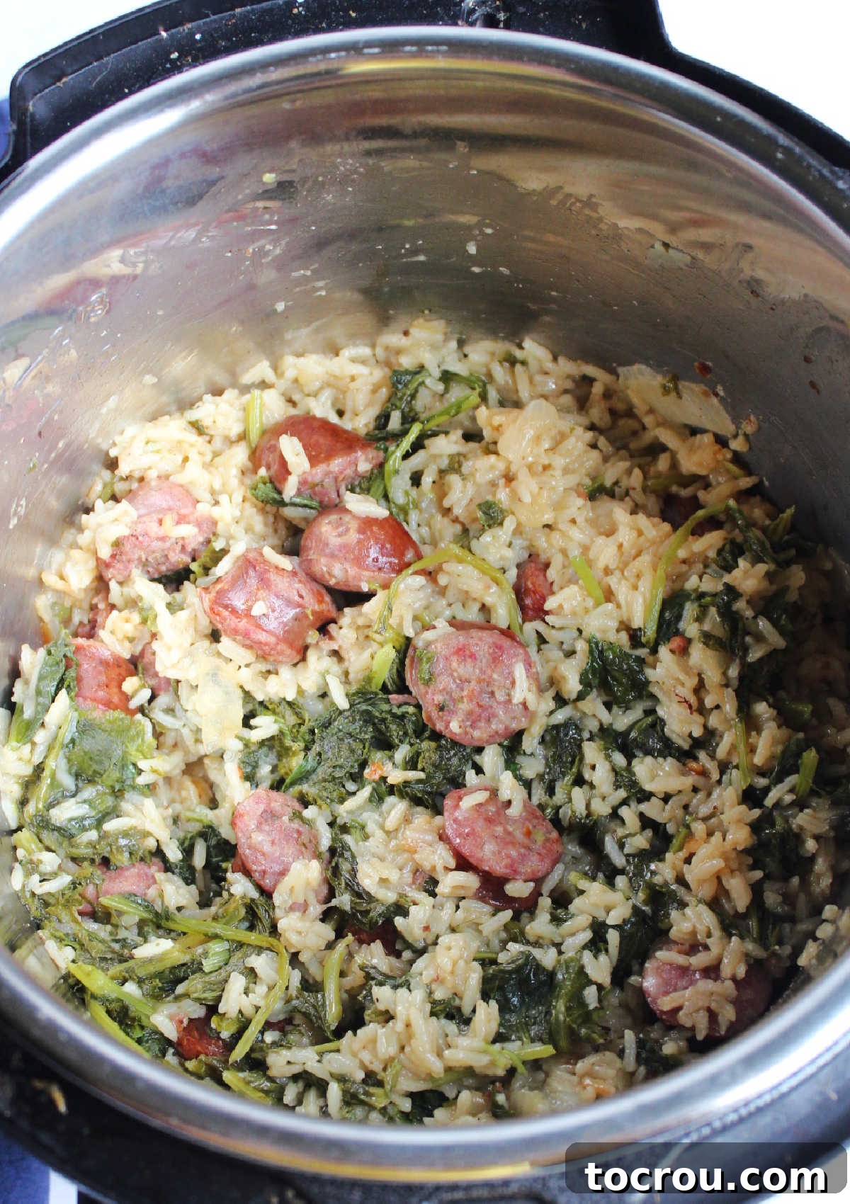 The Instant Pot is open, revealing a perfectly cooked meal of fluffy rice, tender kielbasa, and beautifully wilted mustard greens, all mingling together. The steam gently rises, indicating it's ready to be stirred and served.