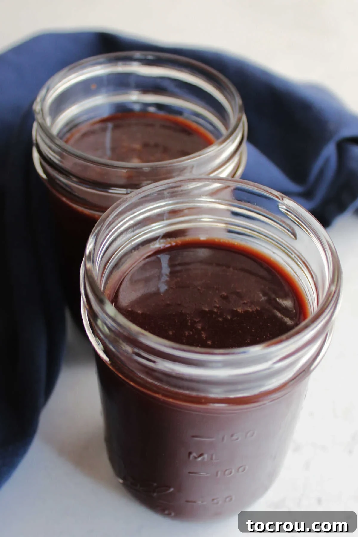 Two glass jars of freshly made hot fudge sauce ready to use.