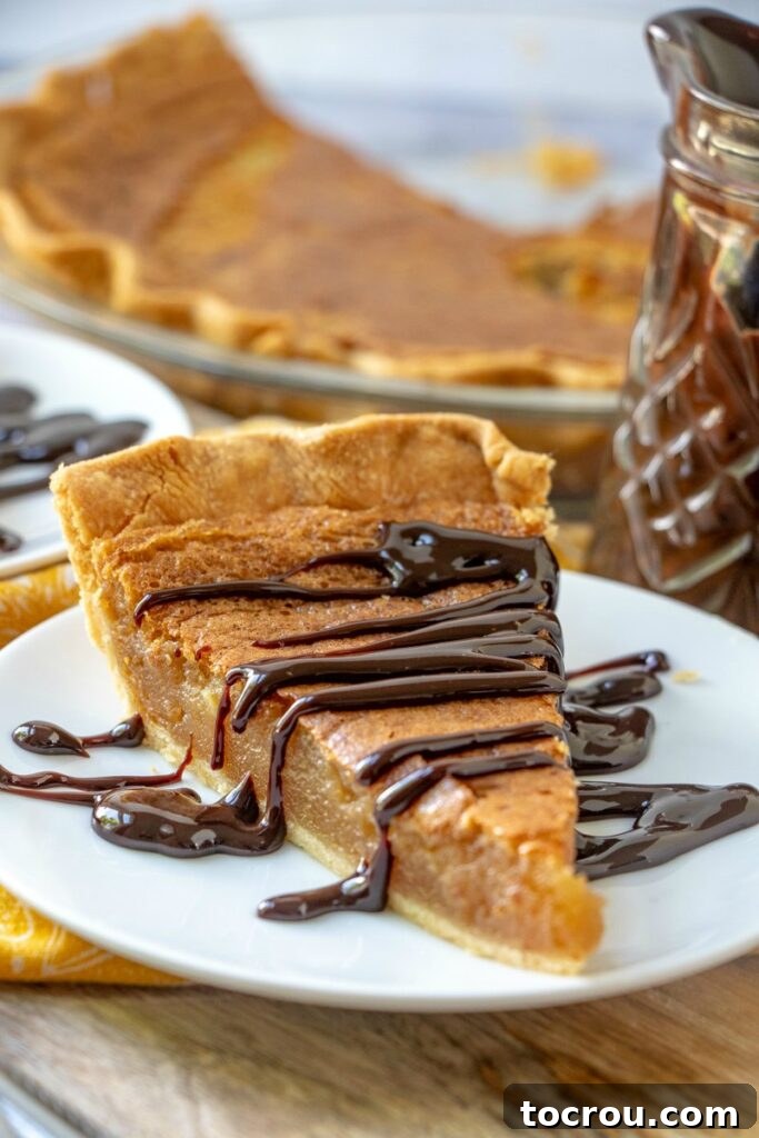 slice of baked peanut butter pie with hot fudge on plate with rest of pie behind it.