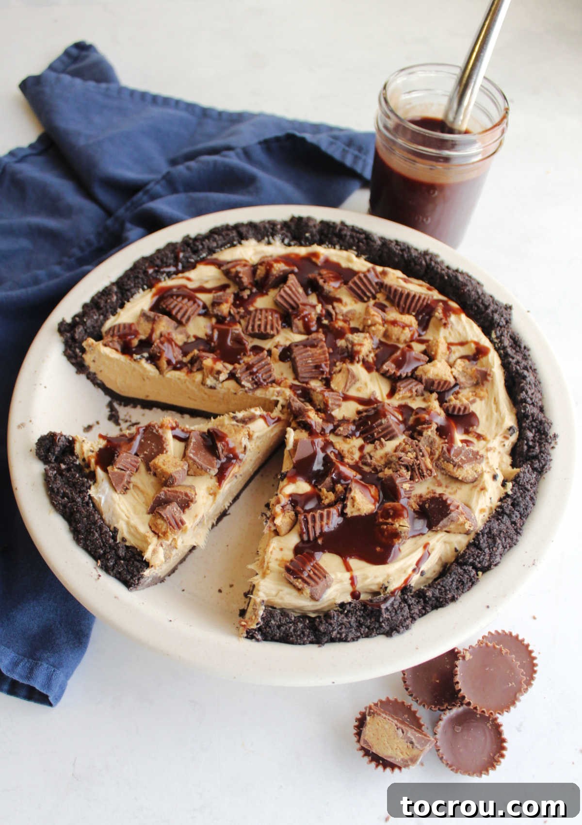 Sliced peanut butter pie with Reese's peanut butter cups and a jar of hot fudge.