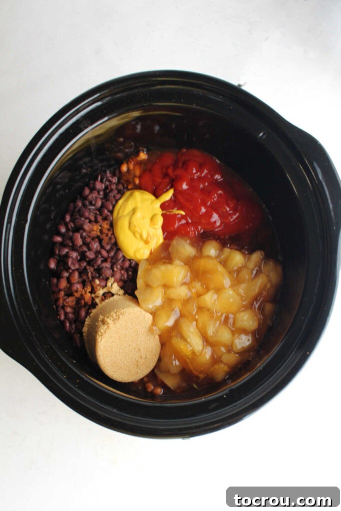 Ultimate Slow-Cooked Baked Beans 4 A slow cooker pot filled with a rich mixture of beans, ketchup, yellow mustard, brown sugar, and chunks of apple pie filling, ready for slow cooking.