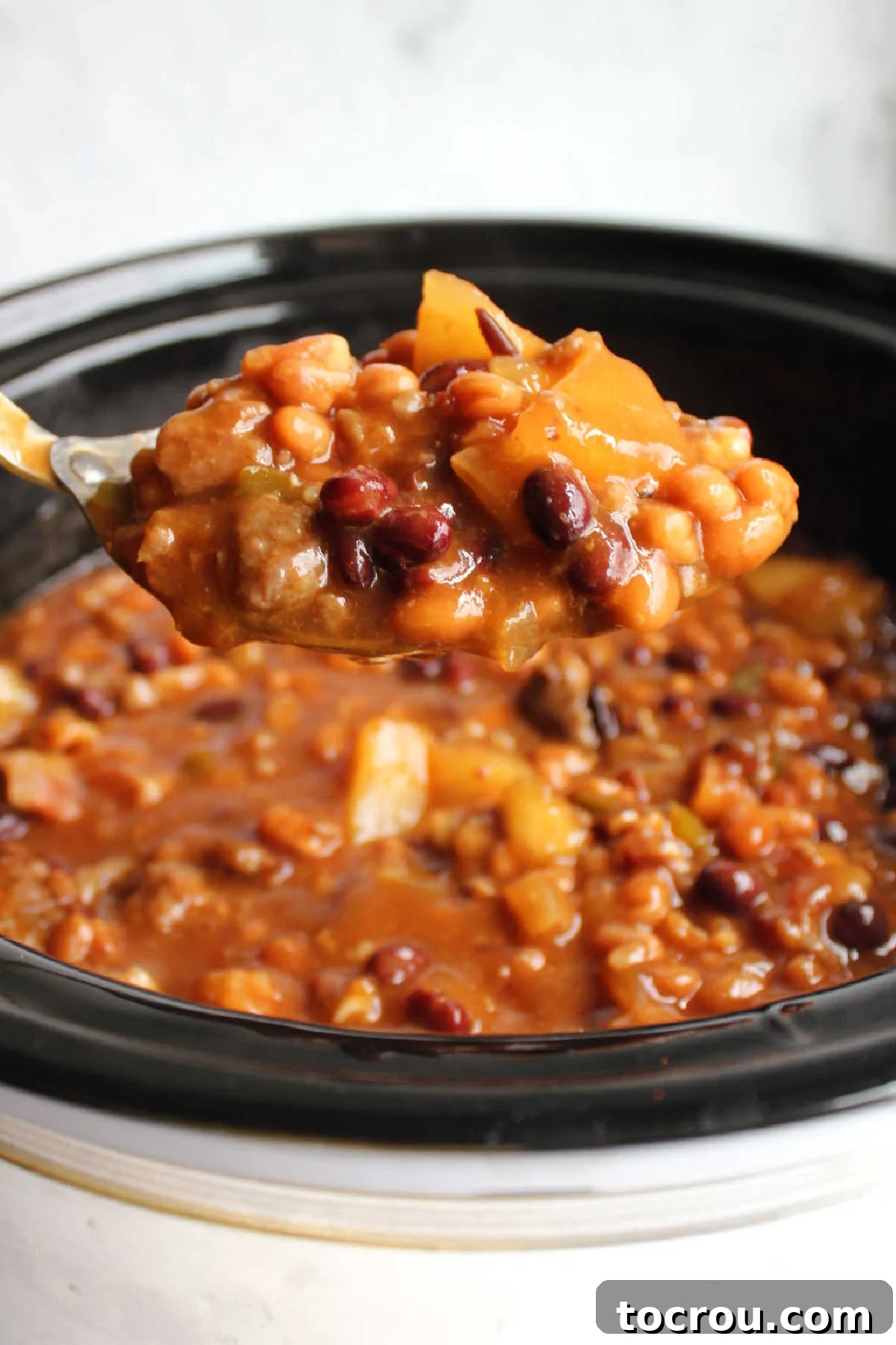 Ultimate Slow-Cooked Baked Beans 6 A serving spoon laden with rich, loaded baked beans, being lifted from a slow cooker, showcasing the delicious blend of ingredients.