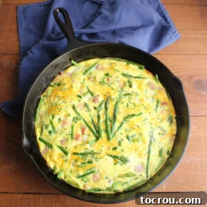 cast iron skillet full of frittata with eggs ham asparagus and cheese.