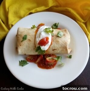 Baked breakfast chimichanga with sour cream, tomatoes and cilantro on top.