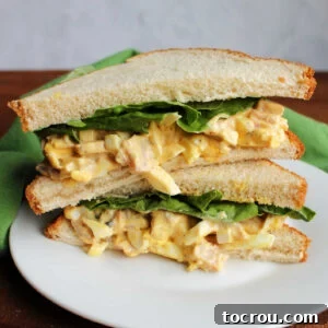 Sandwich with whole wheat white bread, lettuce, and ham and egg salad cut in half.