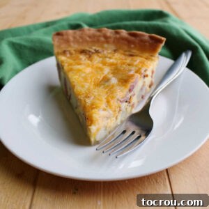 Slice of ham, potato and cheese quiche on plate with fork.