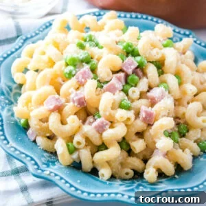 Close up plate of curly pasta with cubes of ham, peas and paremsan cheese.