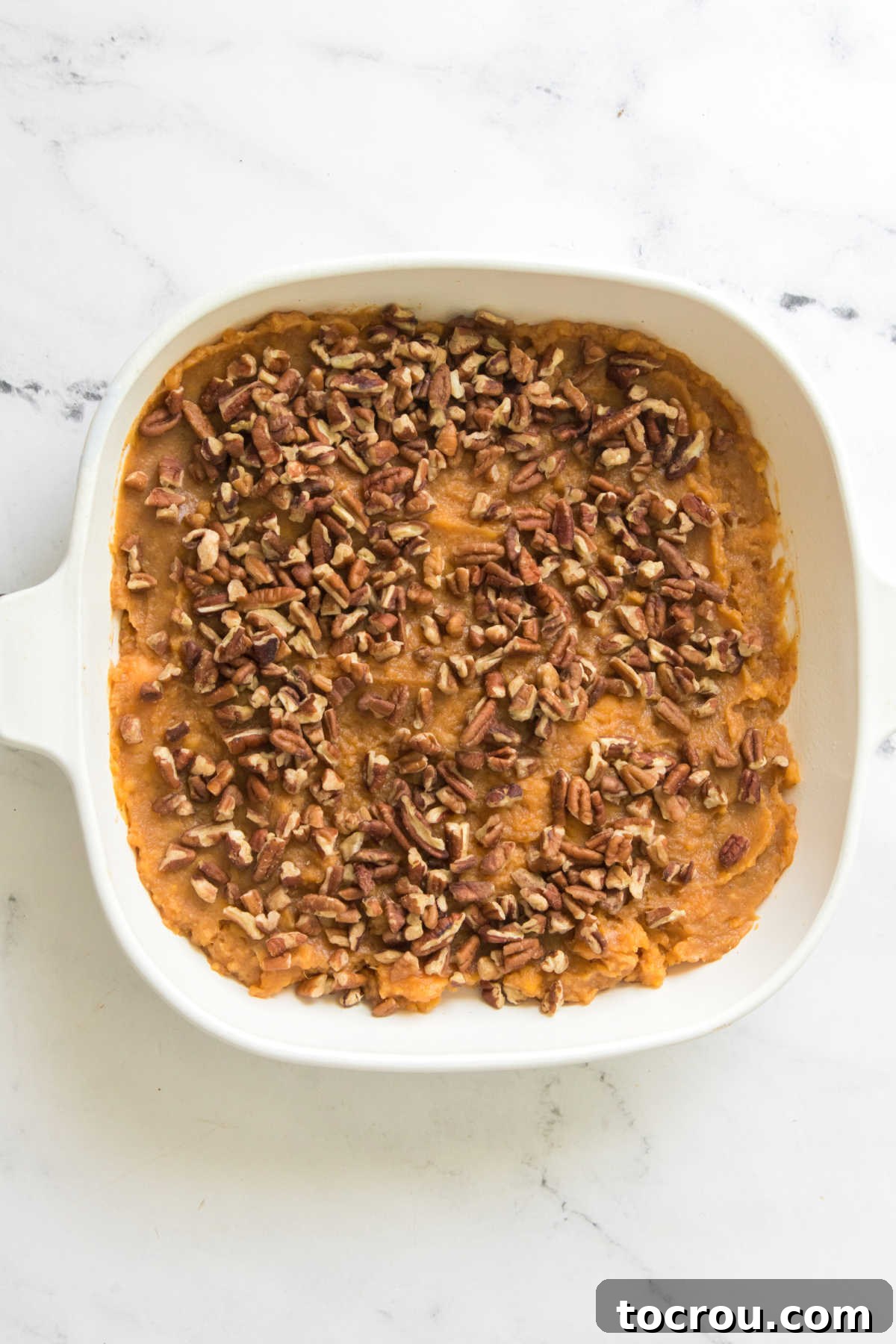 Casserole dish filled with mashed sweet potatoes and sprinkled with pecans.