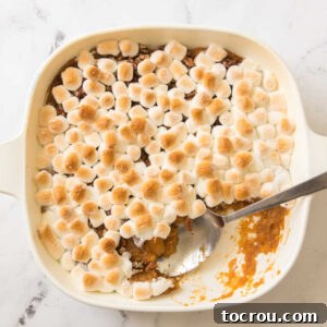 Square casserole dish filled with a layer of mashed sweet potatoes topped with pecans and gold brown marshmallows.