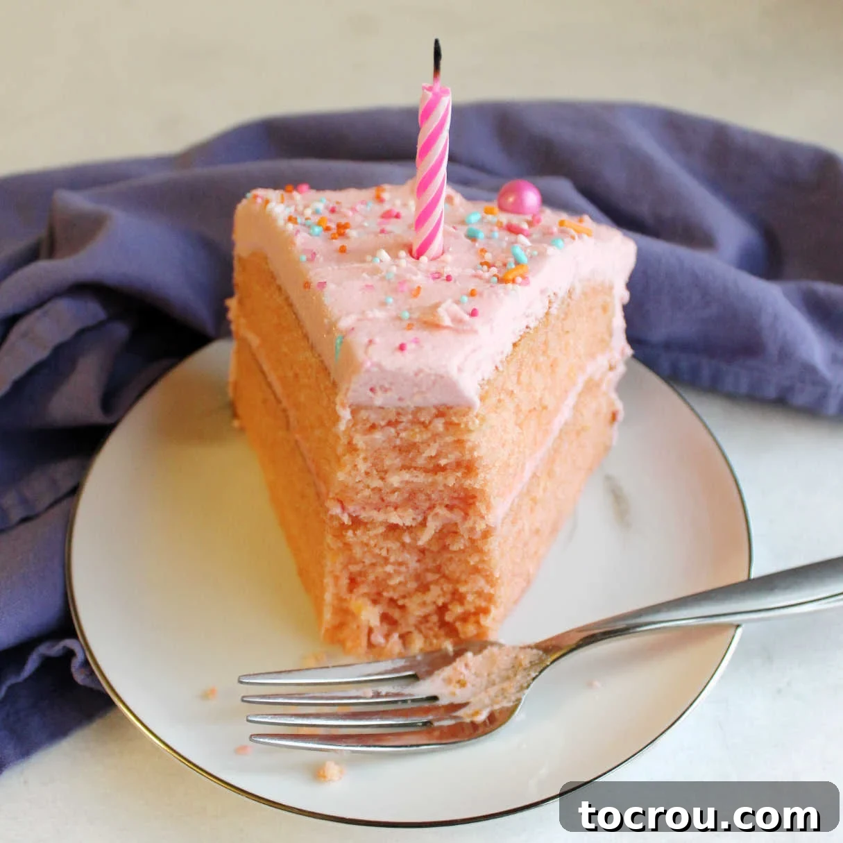 Big slice of pink velvet cake on plate with a bite taken out of the end and a blow out candle on top.