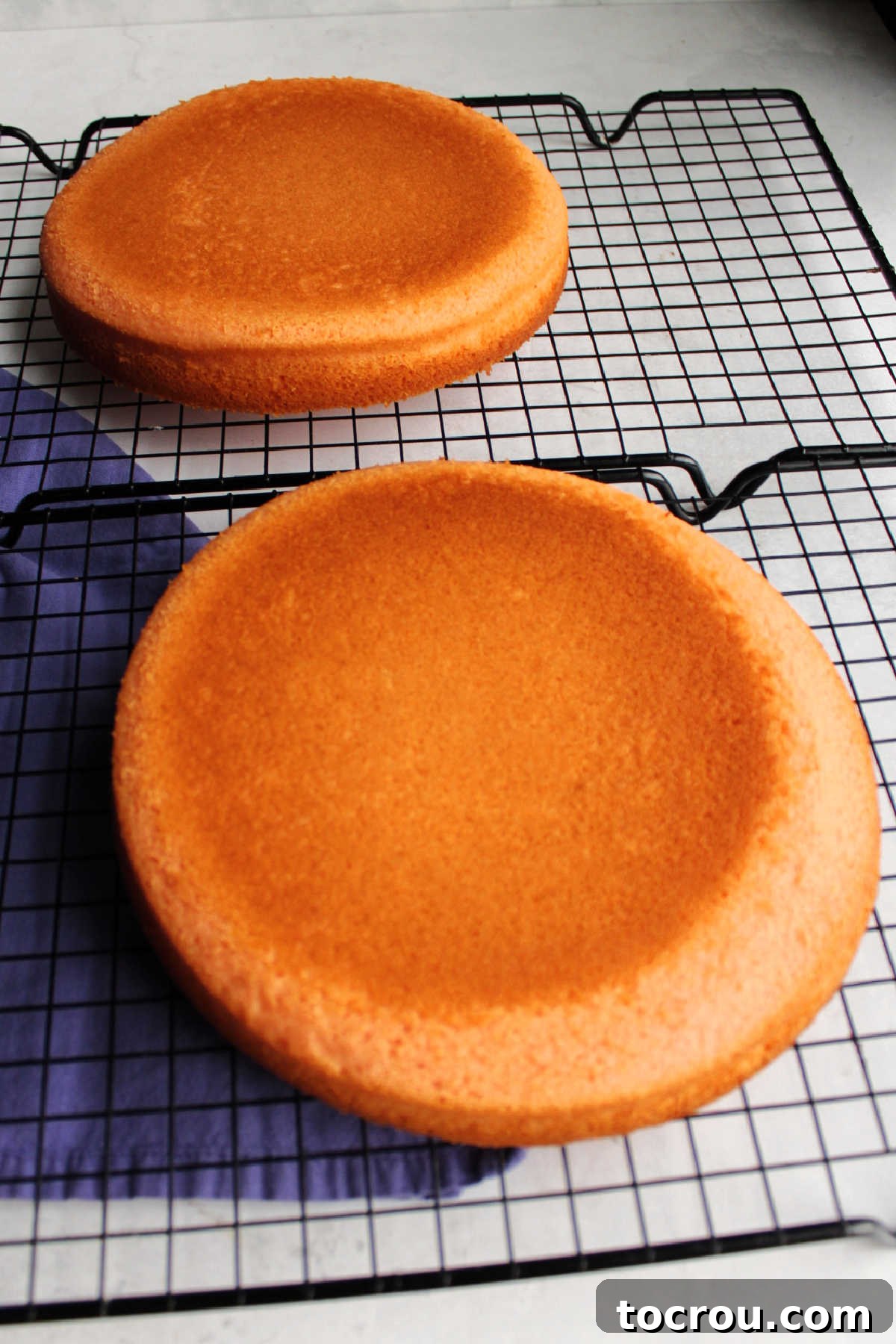 Two round pink velvet cakes cooling on wire racks.