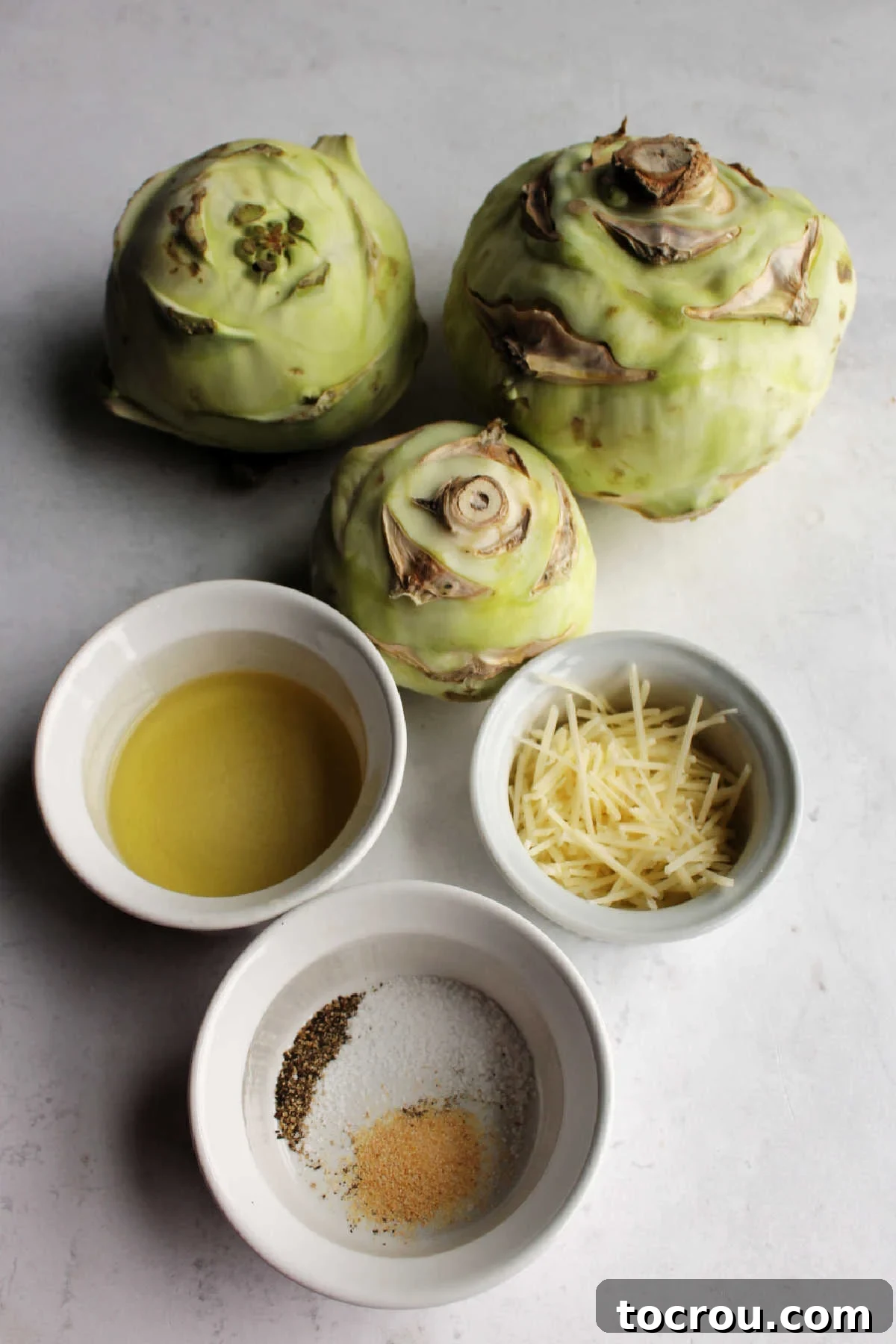 Ingredients for roasted kohlrabi: fresh kohlrabi bulbs, cooking oil, salt, pepper, garlic powder, and grated Parmesan cheese, neatly arranged and ready for preparation.
