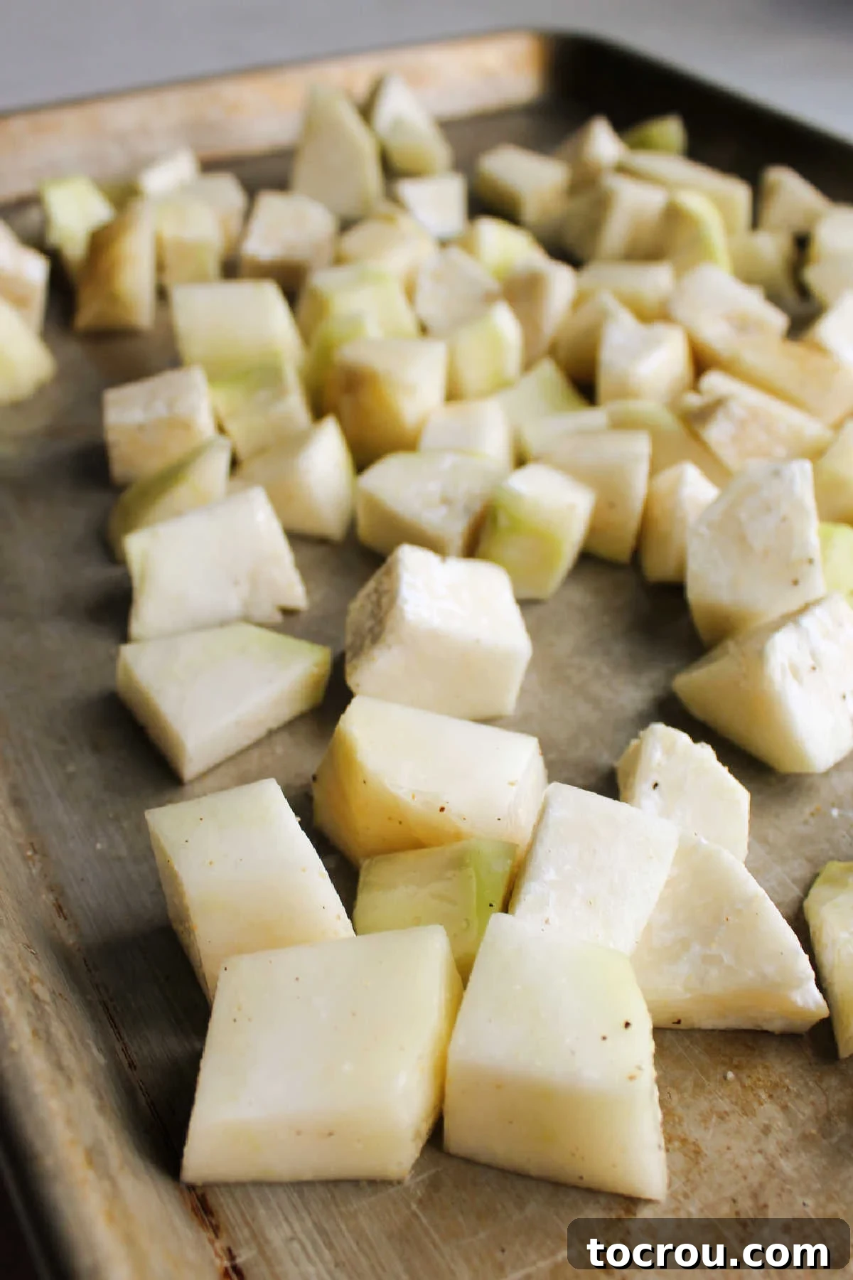 Diced kohlrabi chunks spread evenly on a baking sheet, seasoned and ready for roasting.