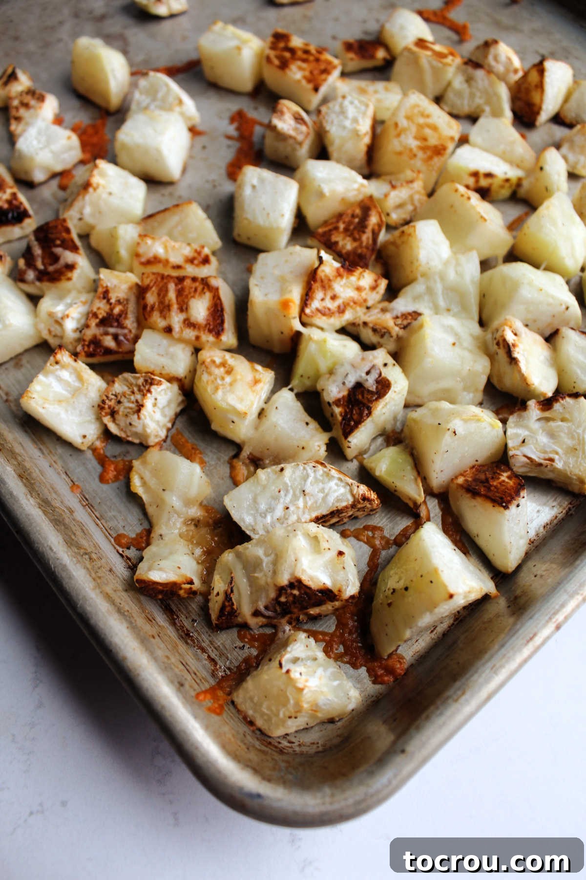 Parmesan cheese perfectly melted and lightly browned over roasted kohlrabi cubes, creating a tempting and flavorful side dish ready to be served.
