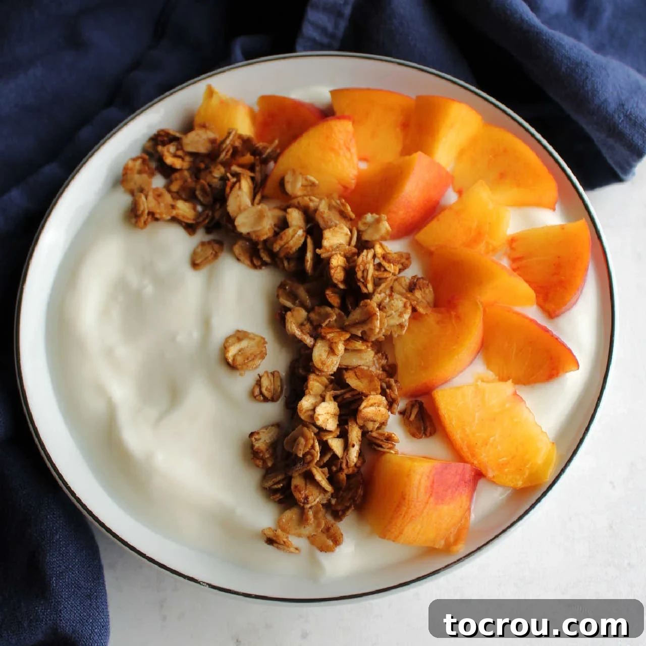 Bowl of yogurt topped with chunks of fresh peach and maple cinnamon granola.