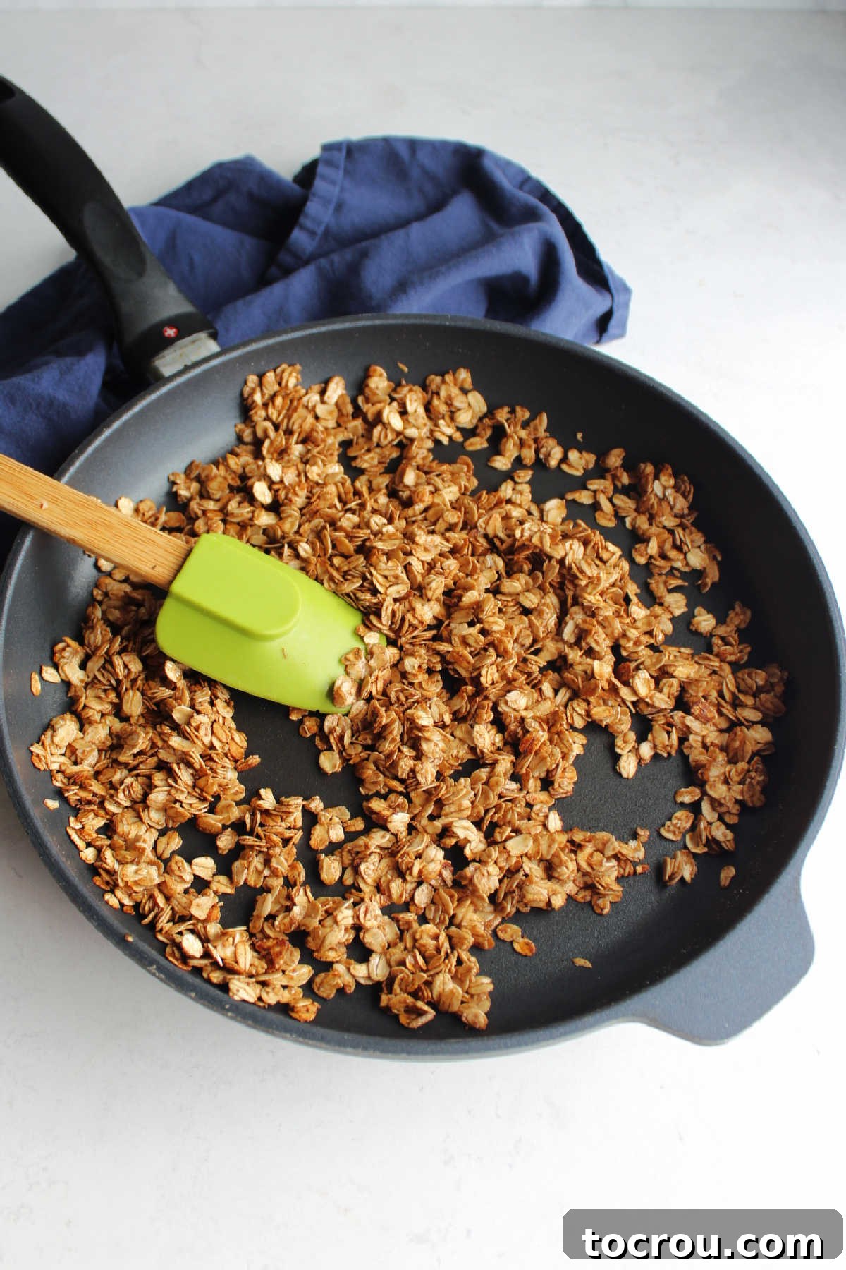 Large skillet filled with freshly make maple cinnamon granola and spatula.
