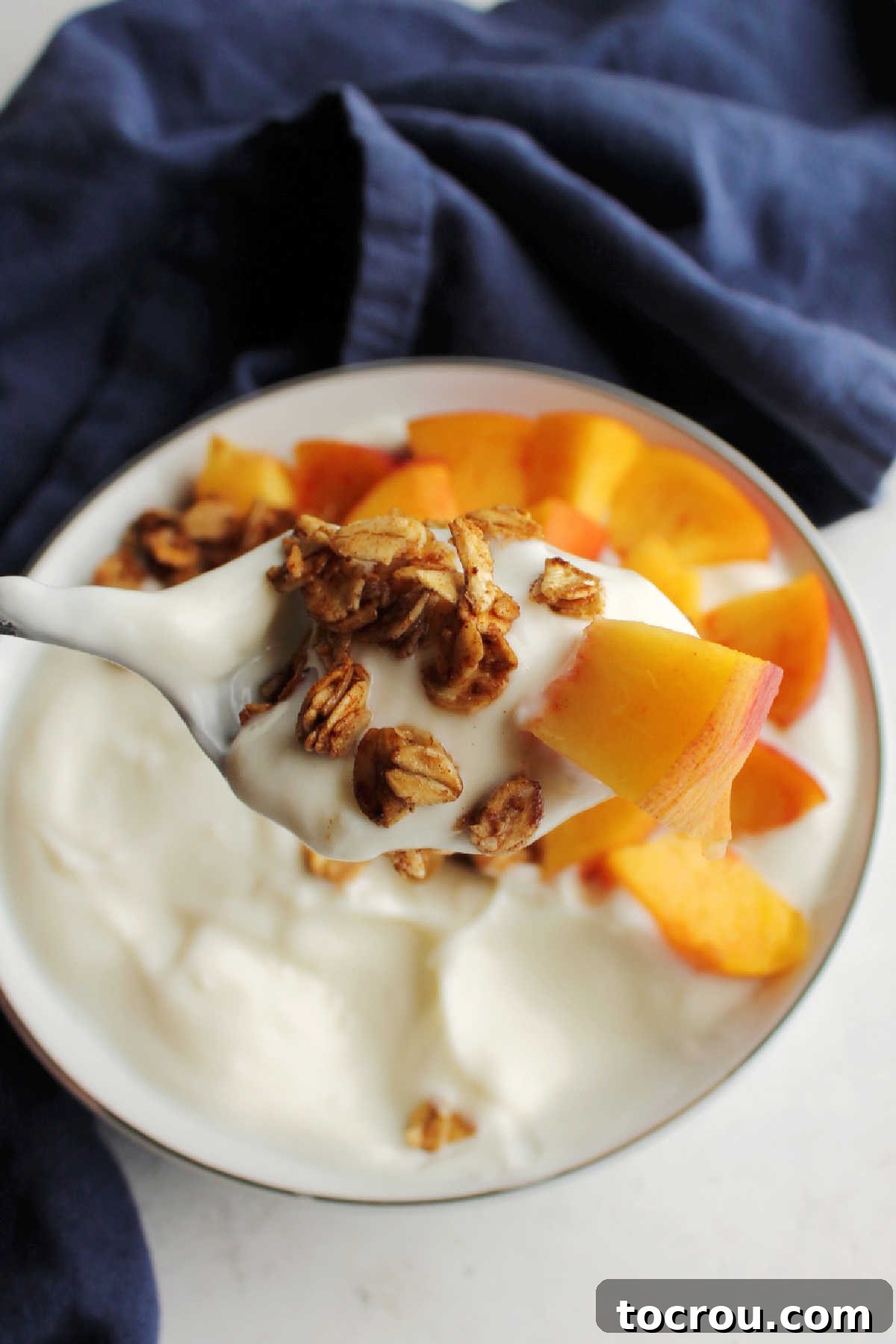 Spoonful of yogurt with skillet granola and a chunk of fresh peach, ready to eat.