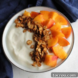 Bowl of yogurt topped with chunks of fresh peach and maple cinnamon granola.