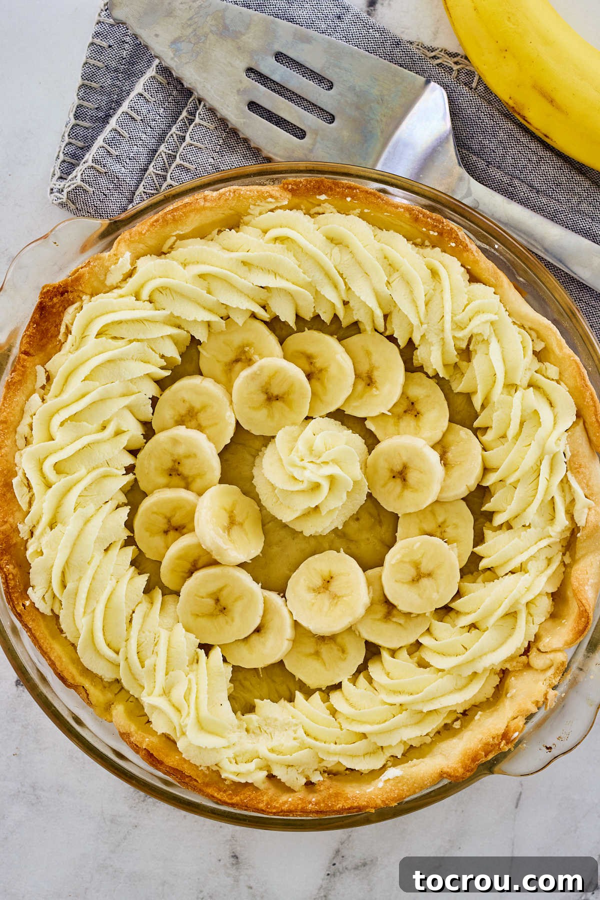 Banana cream pie topped with banana sliced and whipped cream, ready to be sliced and served.
