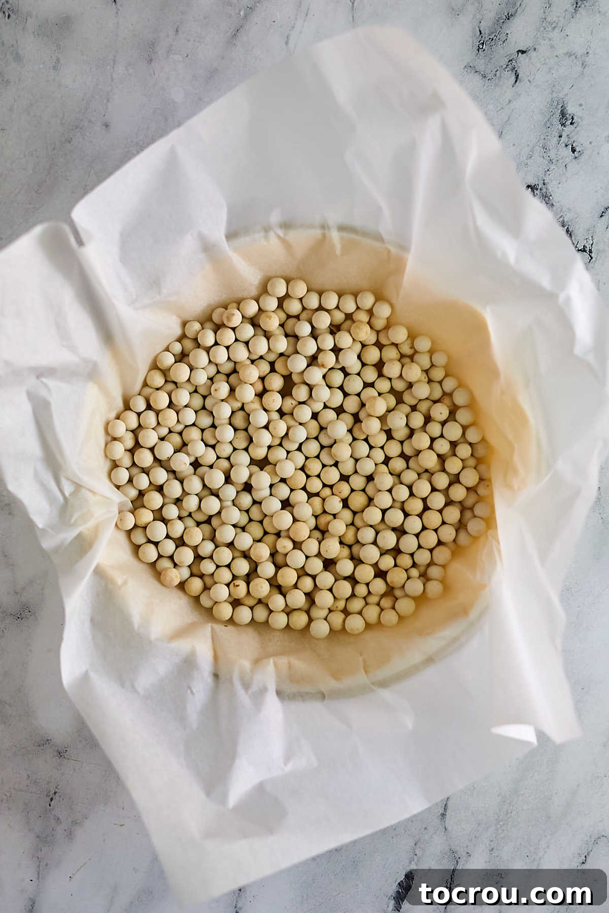 Pie pastry in pie plate filled with parchment paper and pie weights, ready to be blind baked. 