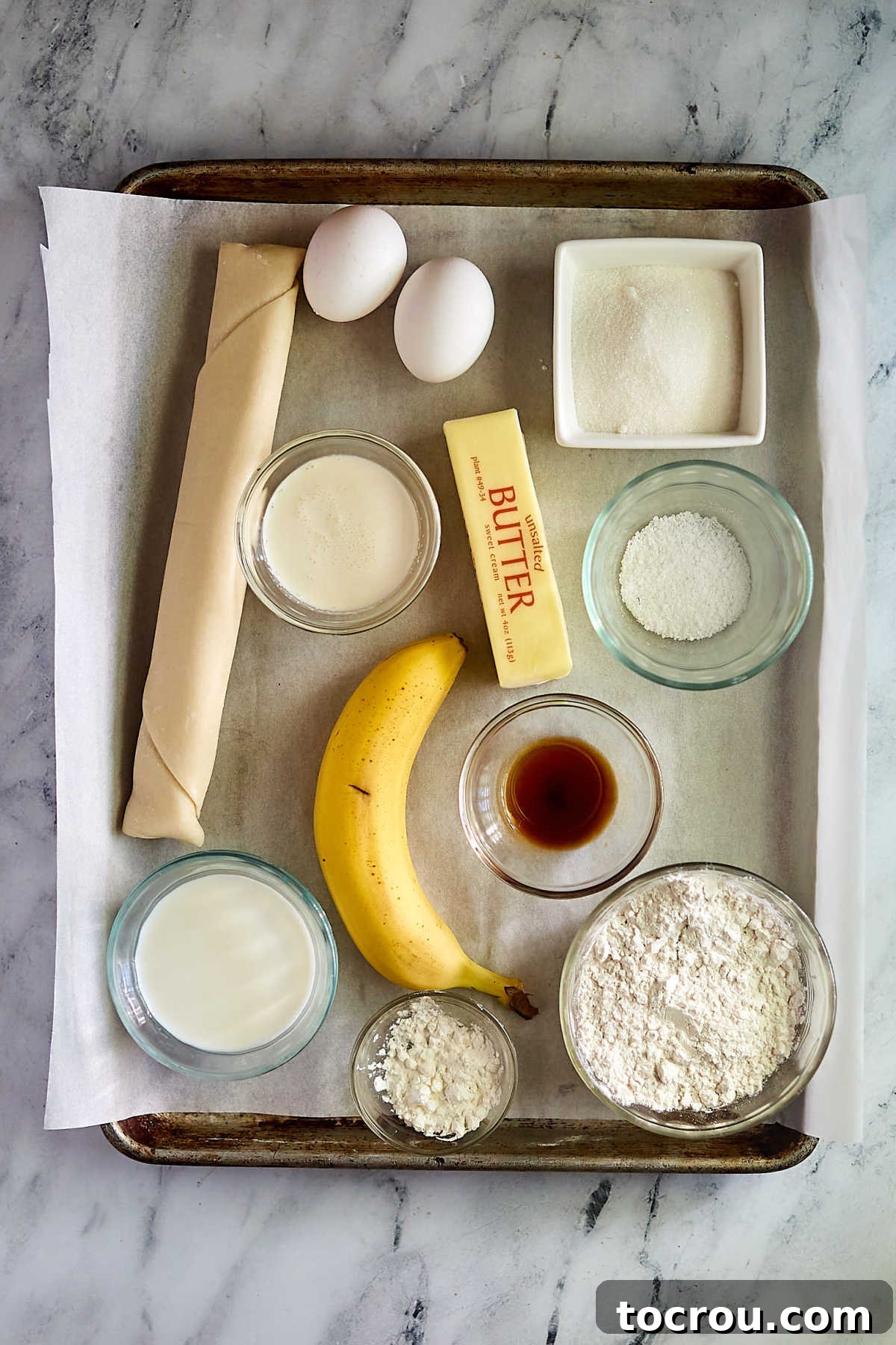 Ingredients including pie pastry, bananas, eggs, milk, butter, cream, flour, cornstarch, and sugar ready to be made into a banana cream pie. 
