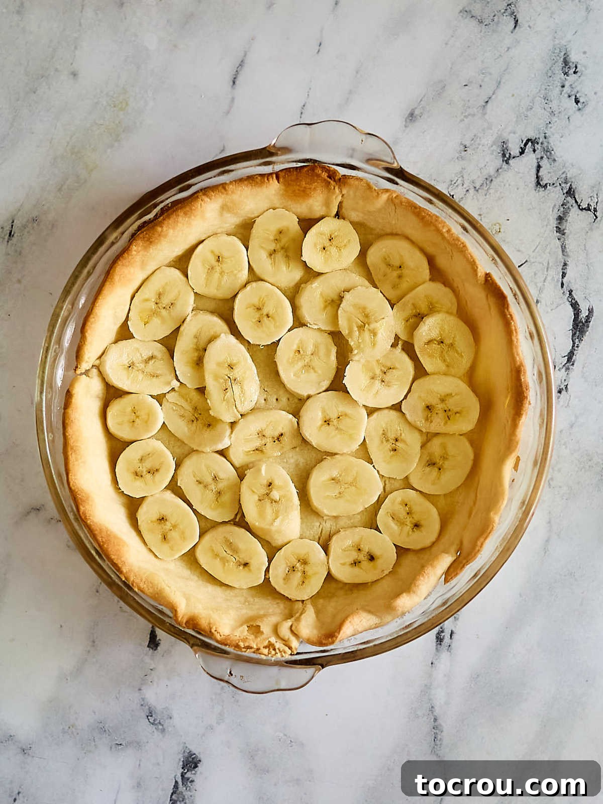 Sliced bananas in the bottom of a golden brown pie crust, ready for pudding. 