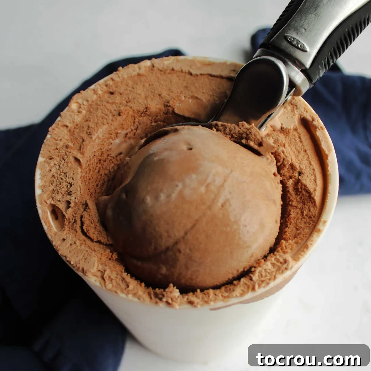 A scoop of homemade chocolate ice cream being lifted from a container, showcasing its smooth and rich texture.