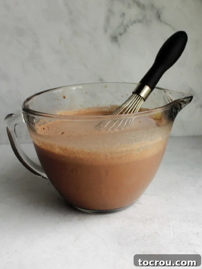 Large glass mixing bowl containing the dark chocolate ice cream base, with a whisk resting inside, ready for chilling.