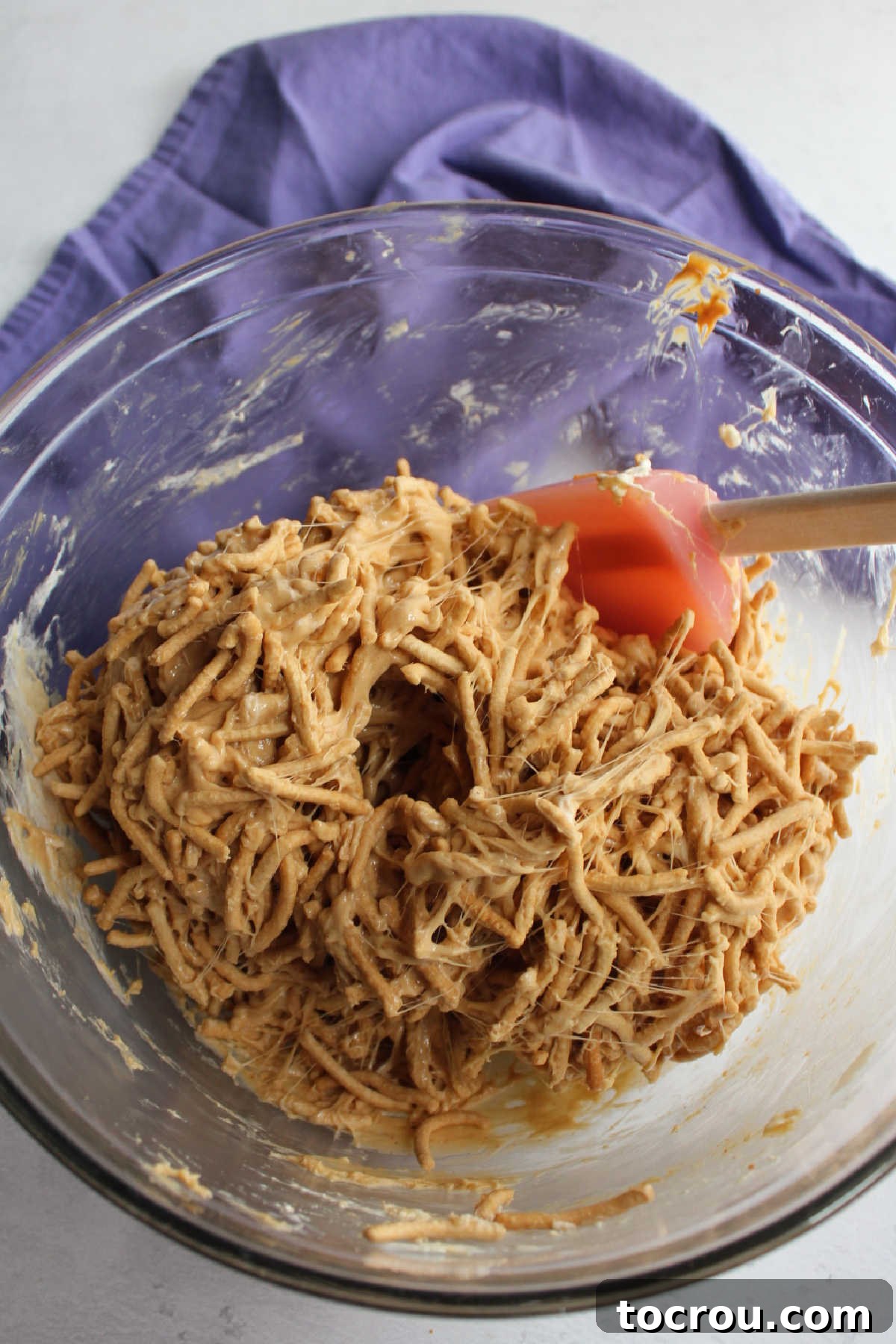 Mixing the Chow Mein Noodle Mixture A large mixing bowl filled with crispy chow mein noodles, thoroughly coated in a rich, glossy peanut butter and marshmallow mixture, perfectly ready to be formed into individual nest shapes.