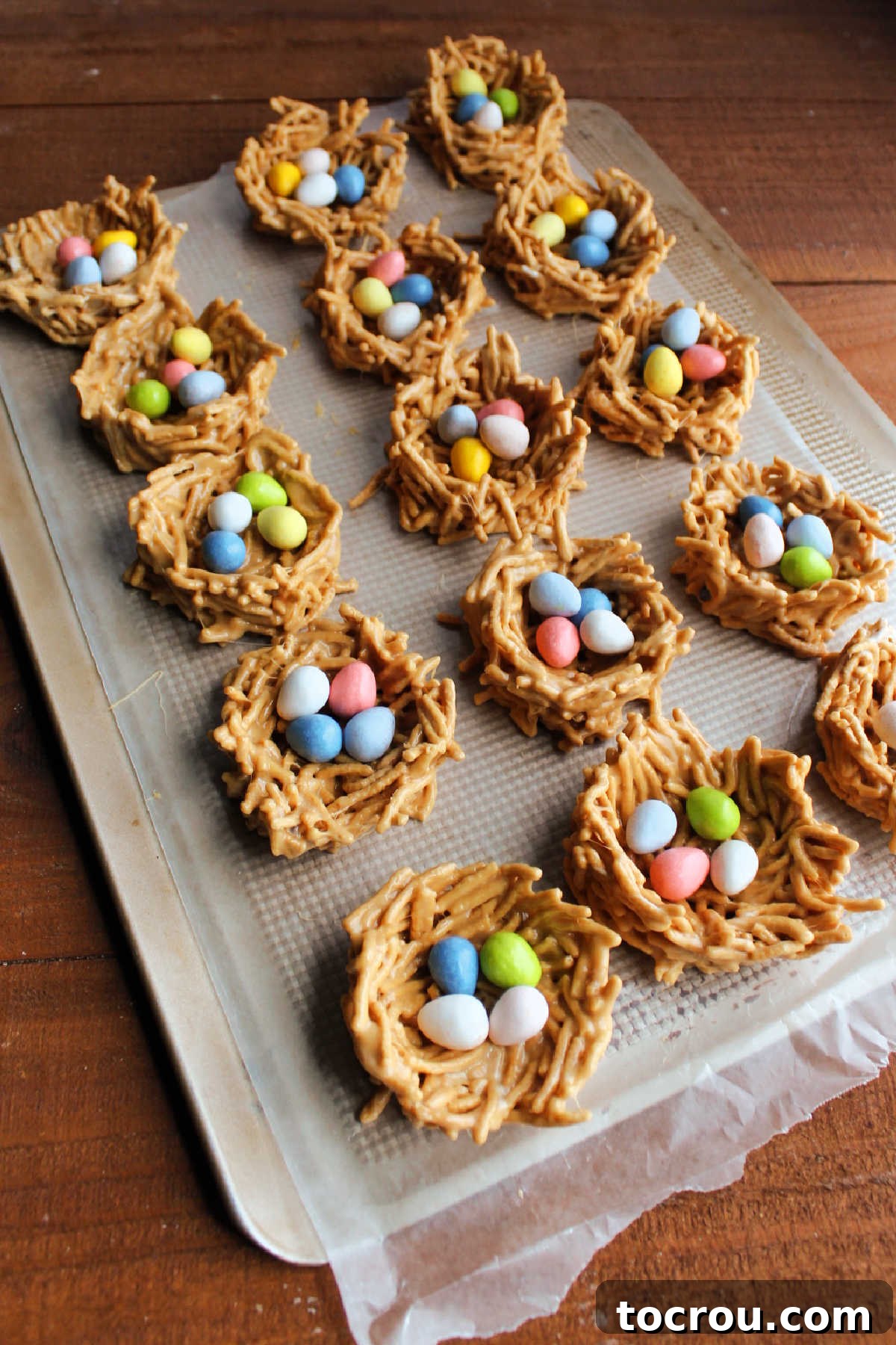 Finished Chow Mein Nests with Candy Eggs A vibrant tray of finished chow mein nests, generously filled with a delightful variety of chocolate and peanut butter candy eggs, making them an extra special and eye-catching treat for Easter celebrations.