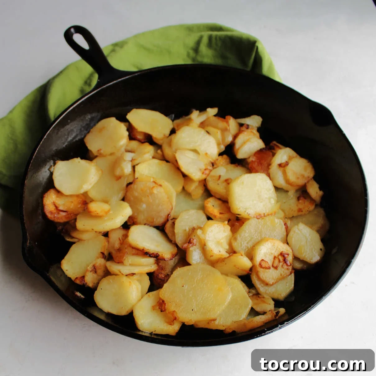 Large cast iron skillet filled with golden brown, crispy fried sliced potatoes, ready to be served.