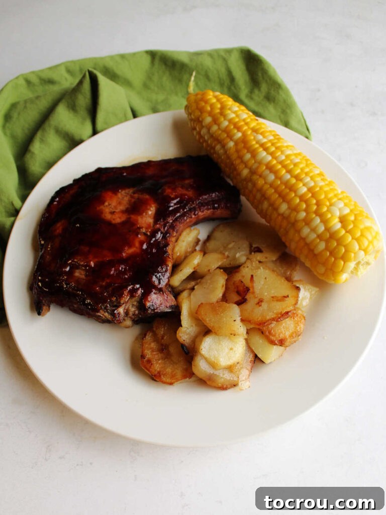 A complete and satisfying meal, showcasing a plate with a generous portion of crispy fried potatoes, a tender barbecued pork chop, and a vibrant ear of fresh corn on the cob.