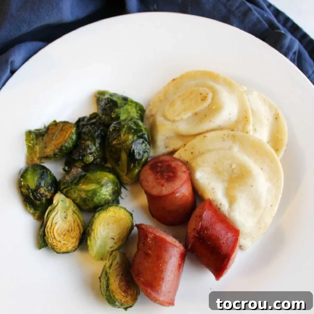 Kielbasa Pierogi Brussels Sprouts Sheet Pan Dinner Dinner plate of sheet pan meal with sausage, pierogies and brussels sprouts, garnished with fresh herbs.