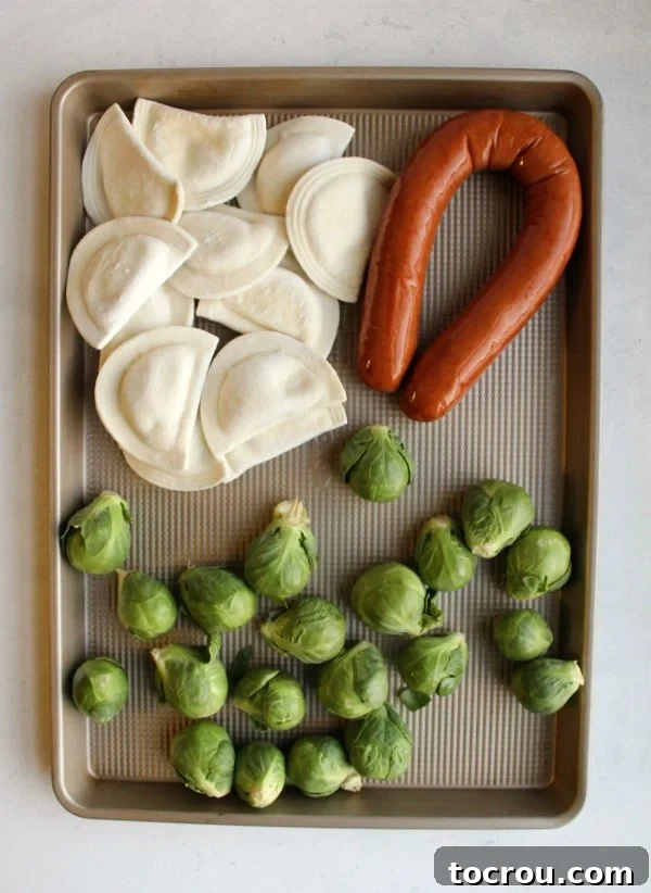 Raw Ingredients on Sheet Pan Uncooked pierogi, whole brussels sprouts, and whole kielbasa sausage on a sheet pan before roasting.
