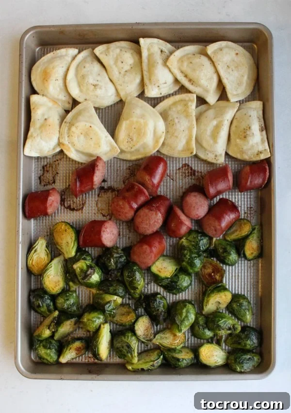 Cooked Sheet Pan Meal Cooked pierogi, hunks of sausage, and halved brussels sprouts on a sheet pan after roasting, showing browned edges.