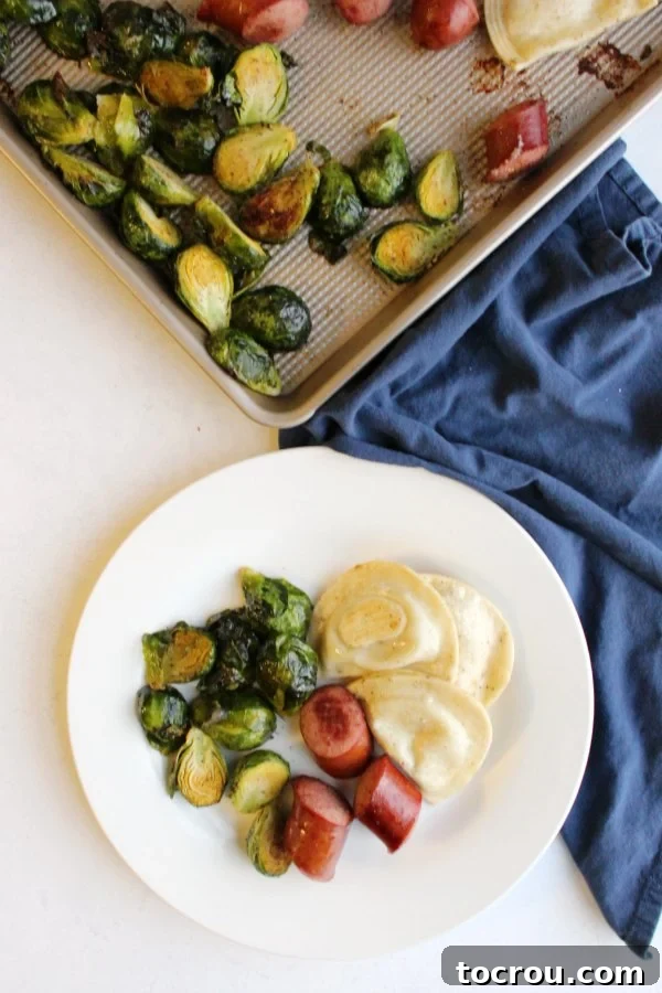 Plate of Kielbasa Pierogi Brussels Sprouts Chunks of polish sausage, brussels sprouts, and pierogi on a plate with sheet pan they were cooked on in the background.