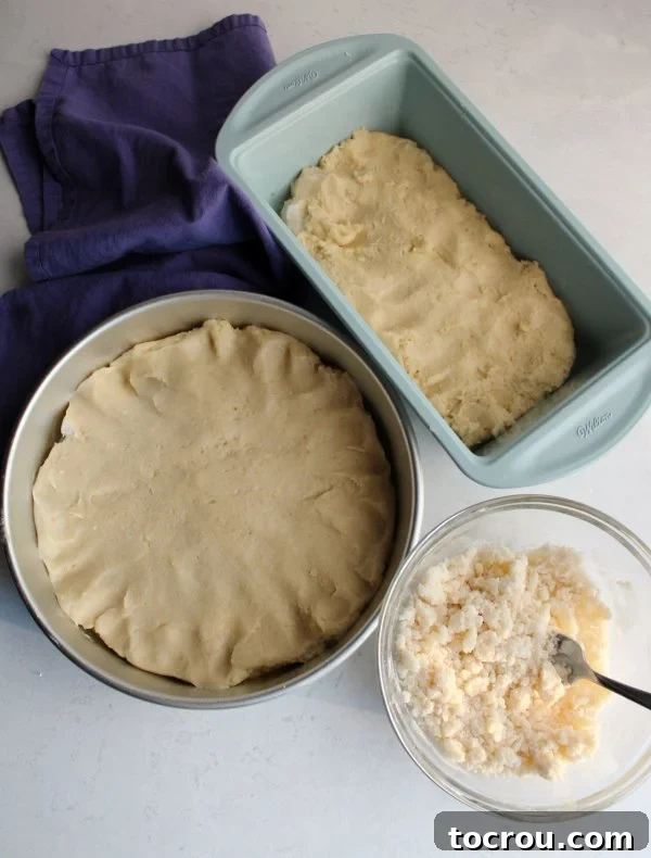 Placek dough rising in pans, awaiting its delicious crumb topping. Two baking pans filled with Placek dough, rising, next to a bowl of crumb topping (Kruszynki) ready to be sprinkled.