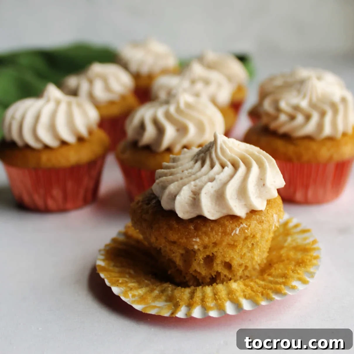 Apple butter mini cupcake unwrapped showing soft cake bottom topped with swirl of apple butter frosting.