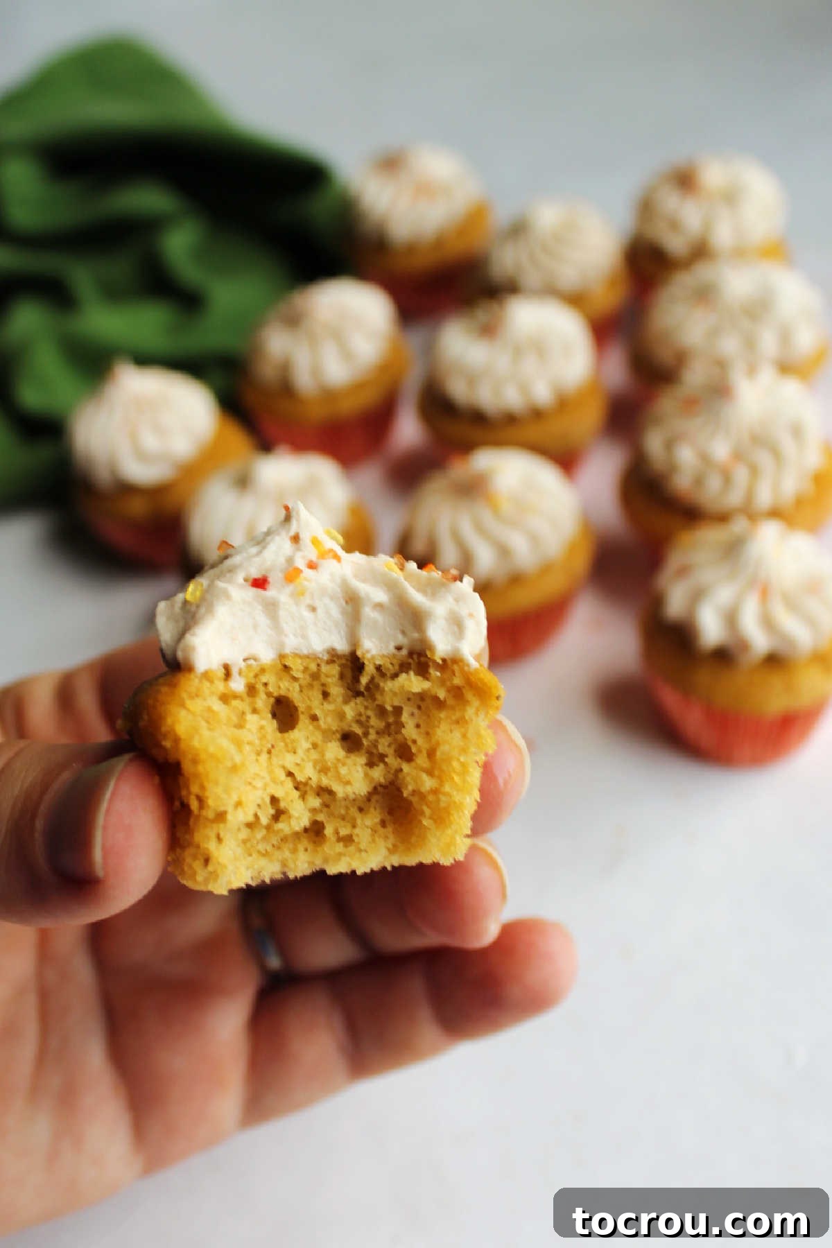 Hand holding mini apple butter cupcake with a bite taken out showing soft tan center.