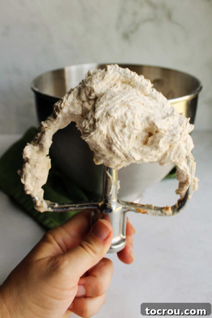 Hand holding mixer paddle filled with fluffy apple butter buttercream.