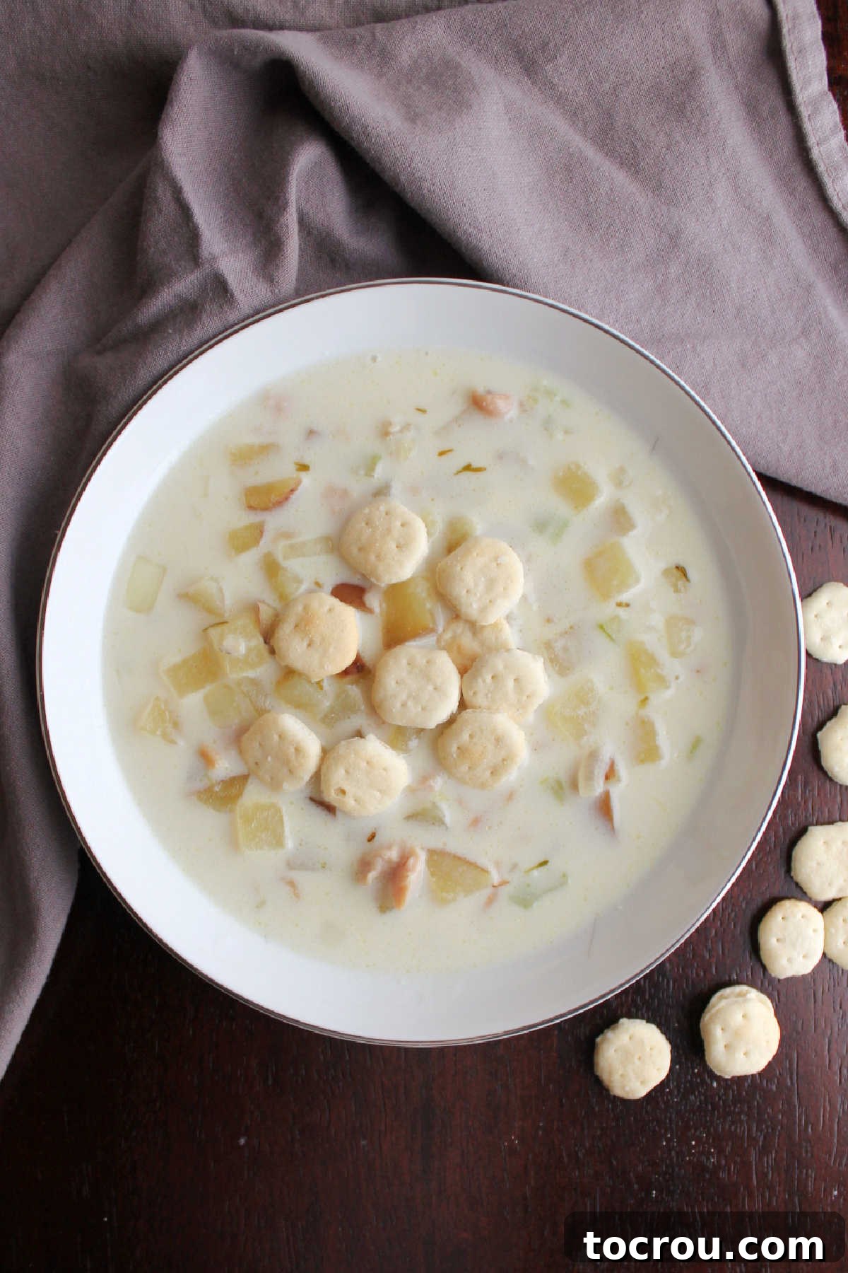 bowl of New England clam chowder with creamy broth, chunks of potatoes, and clams, topped with soup crackers.