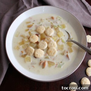 close up of spoon in bowl of creamy New England clam chowder with oyster crackers, ready to enjoy.